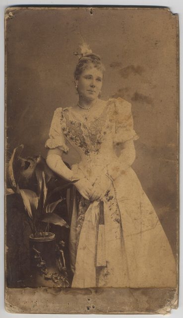 Retrato de una mujer con vestido blanco apoyada sobre un sillón