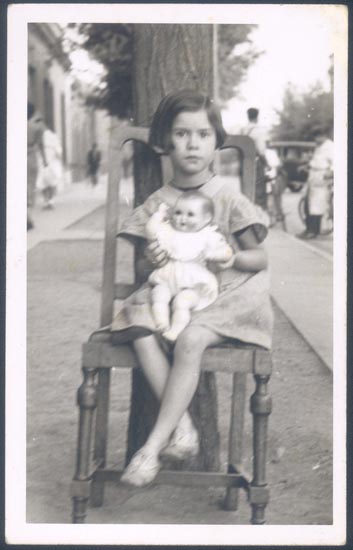 Niña sentada en la calle con su muñeca.